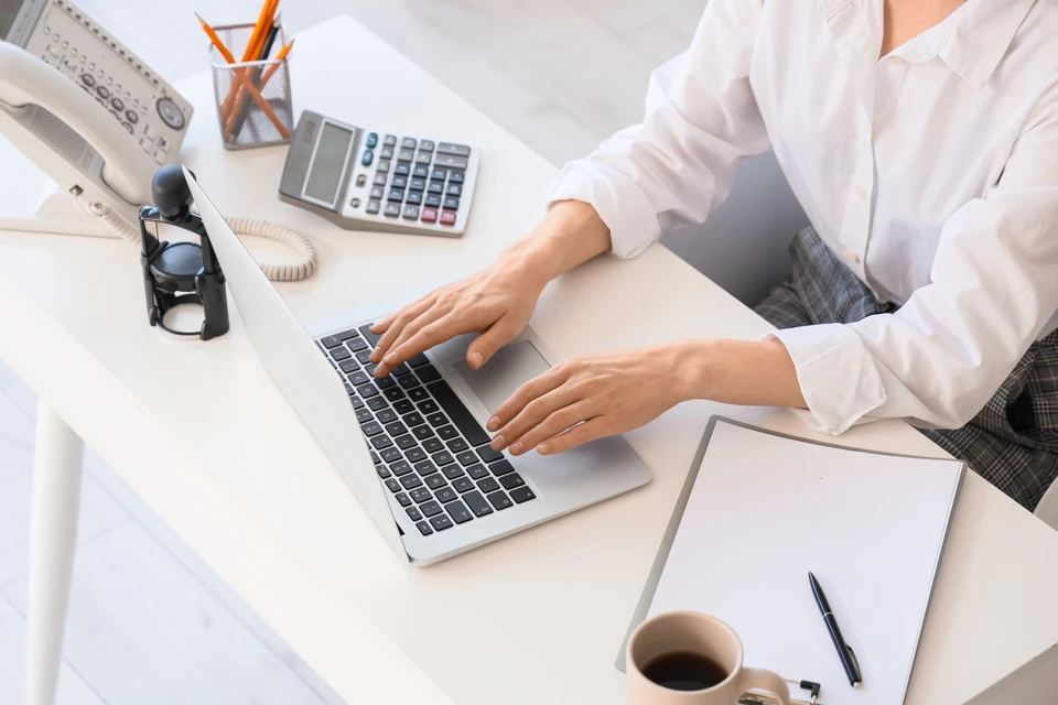 Photographie d'une personne assise à un bureau dans un environnement professionnel, accueillant un client ou occupée à des tâches administratives. L'arrière-plan peut montrer un bureau organisé avec ordinateur et documents. L'image doit transmettre la disponibilité, le professionnalisme et la confiance, reflétant le rôle de référent administratif et de coordination client.